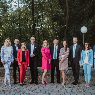 Eine Gruppe von Personen in Geschäftskleidung posiert lächelnd vor einem Wald.