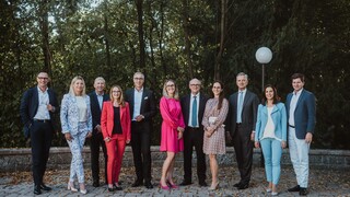 Eine Gruppe von Personen in Geschäftskleidung posiert lächelnd vor einem Wald.