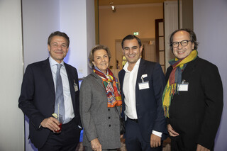 Eine Frau und drei Männer lächeln in die Kamera.