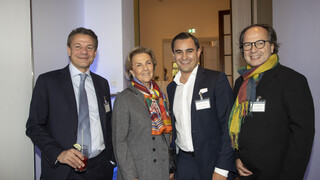 Eine Frau und drei Männer lächeln in die Kamera.