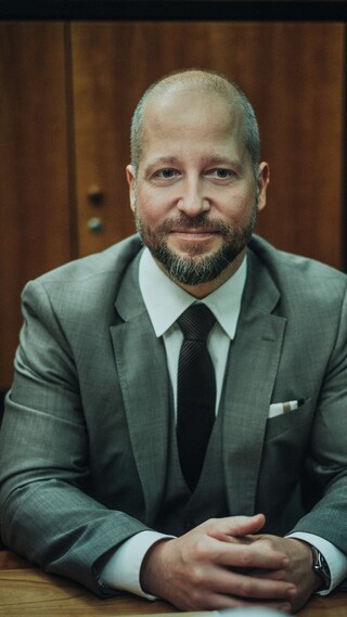 Ein lächelnder Herr in Geschäftskleidung sitzt an einem Tisch.