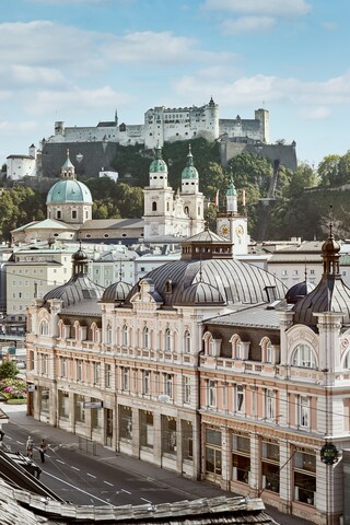 Stammhaus des Bankhaus Spängler in der Schwarzstraße 1 in 5020 Salzburg von außen. Die Fassade ist hellrosa, auffällig ist das Kuppeldach. Im Hintergrund sieht man die Festung Hohensalzburg sowie die Kuppeln des Salzburger Doms. 