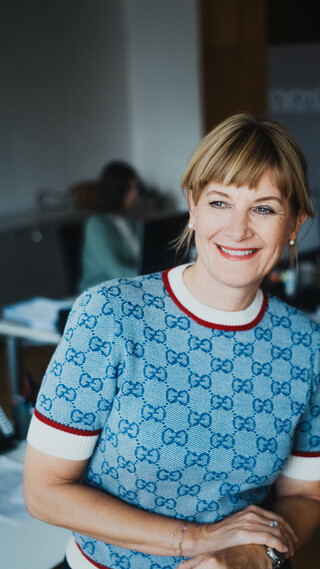 Eine lächelnde Dame in Pullover posiert in einem Büro.