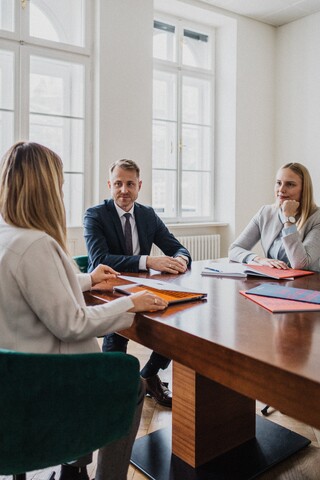Drei Personen sitzen an einem Tisch und besprechen etwas.