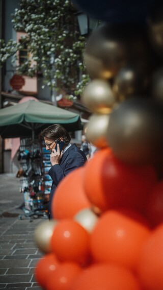Ein Herr in Anzug telefoniert hinter einem Gebilde aus Luftballons.