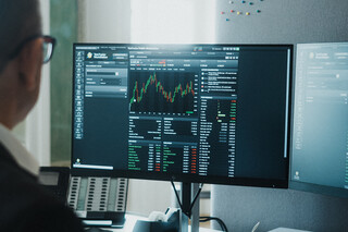 Ein Herr in Geschäftskleidung sitzt vor einem Computerbildschirm mit finanzmathematischen Darstellungen.