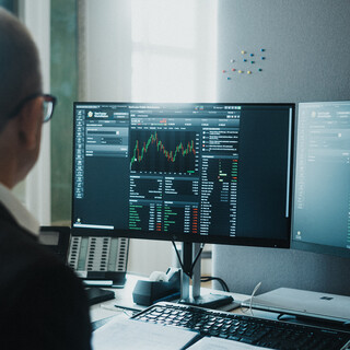 Ein Herr in Geschäftskleidung sitzt vor einem Computerbildschirm mit finanzmathematischen Darstellungen.